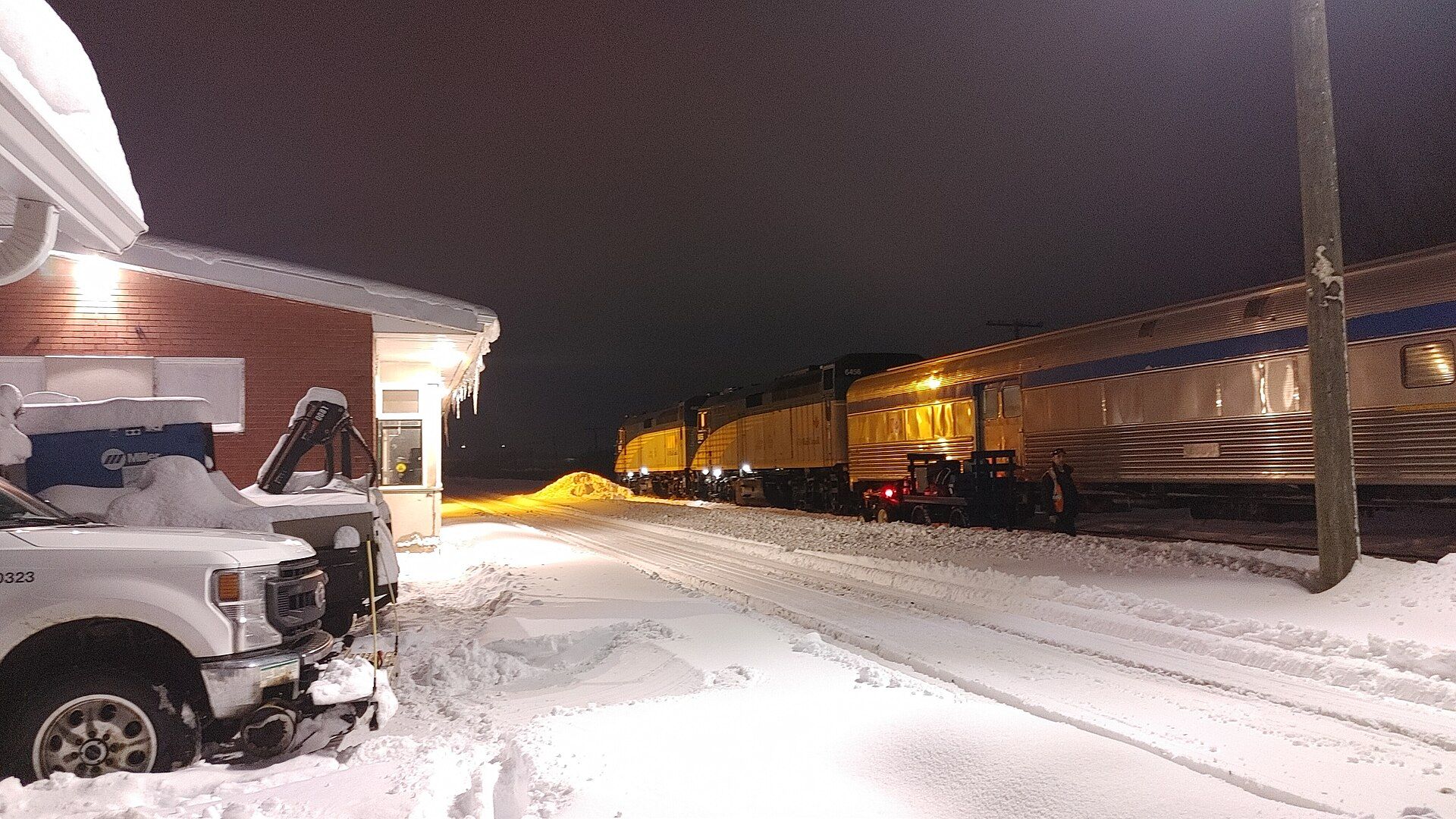Snow falling at night at Sudbury Junction station, a train under the platform lights